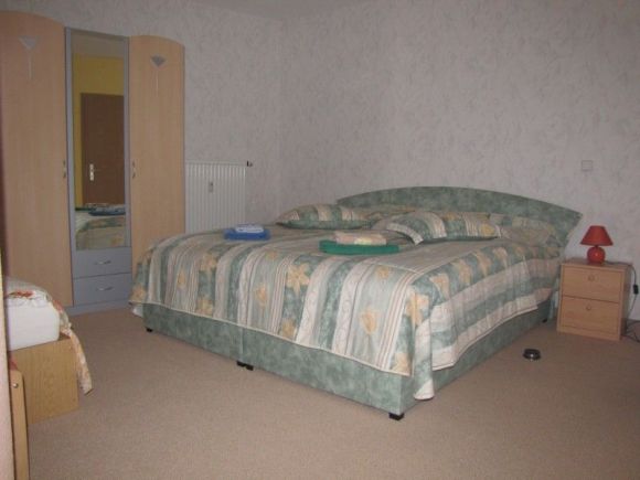 Schlafzimmer mit Doppelbett, Schrank, Nachtschränkchen und am linken Rand eine Aufbettung