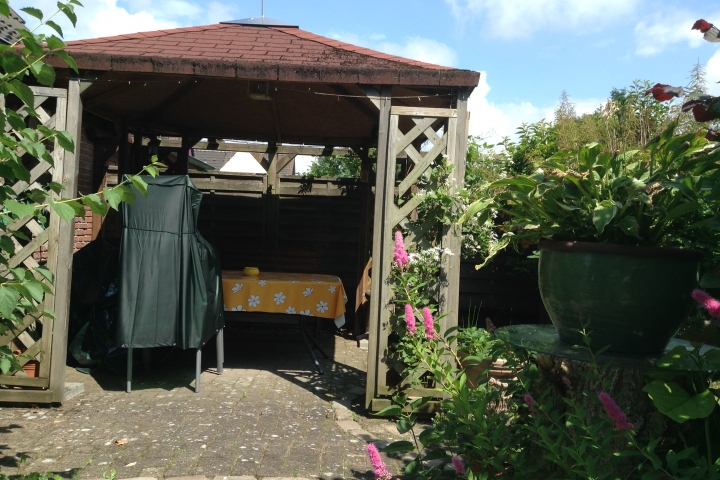 Überdachte Terrasse im Garten mit gemütlicher Sitzecke.