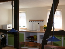 Blick vom Esszimmer in die gemauerte Küche: mit Herd, Kühlschrank, Microwelle, Wasserkocher und Kaffeemaschine.