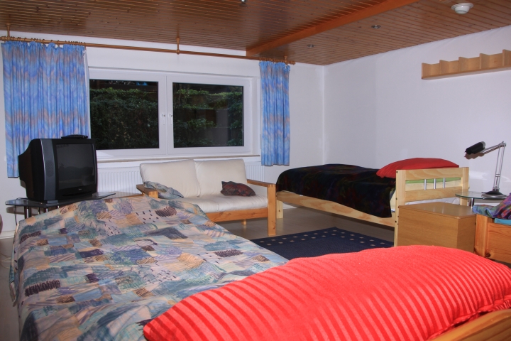 Wohn- und Schlafzimmer 2 (36qm) mit 3 Einzelbetten, Sofa und Fernseher. Bei Bedarf kann ein 4. Bett aufgestellt werden.