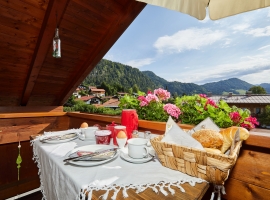 Auf dem überdachten Balkon das Frühstück geniesen und den Sonnenaufgang beobachten - Blick zum Dorf mit Bergpanorama