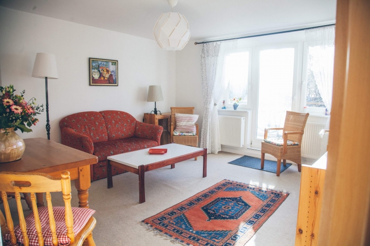 Ferienwohnungen im Gutshaus Neuhof | Wohnzimmer mit Süd Balkon und Markise, Schlafsofa. Die Wohnräume haben einen Tretfort Teppichboden.