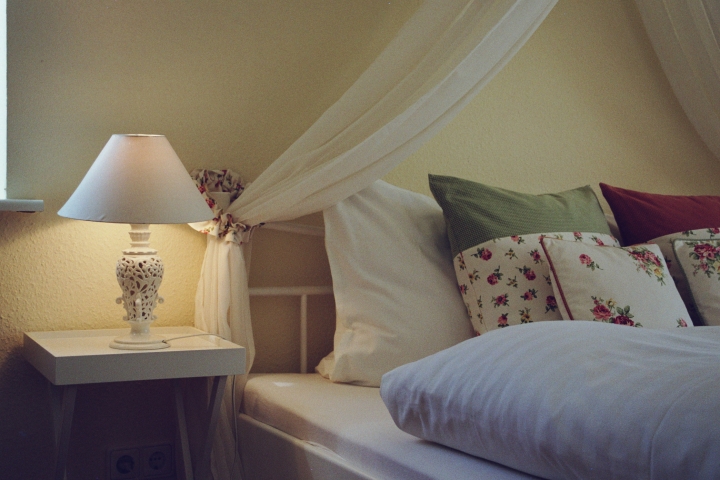 Das romantische Schlafzimmer mit einem weißen Metallbett und eingefasstem Betthimmel.
Ebenso hochwertigen Stores und Seitenschals mit Rosendekor.