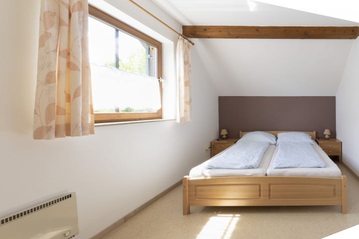 Das sehr große und helle Schlafzimmer mit einem Doppelbett, einem Einbauschrank, sowie einem großen Tisch.