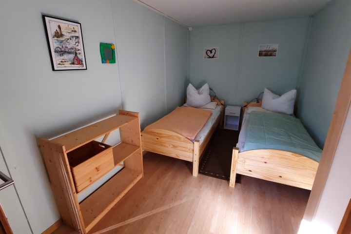 Im Schlafzimmer sind 2 Einzelbetten, Kleiderschrank, Nachttisch und Regal.