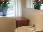 Das Bad mit Fenster. Eckbadewanne und Handtucktrockner gegenüber des Waschbeckens.