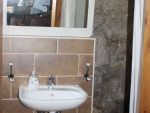 Das kleine Bad mit Waschbecken, offener Dusche, WC und Handtuchtrockner und naturbelassenen Sandsteinwänden.