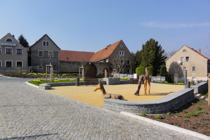 Dorfplatz mit Kletterpferden und Brunnen, im Hintergrund unser Dreiseitenhof