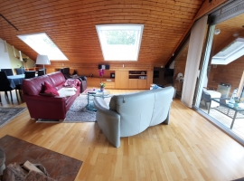 Das Wohnzimmer, mit Eßtisch. Von der offenen Küche aus fotografiert, mit vorgelgertem Verglasten Balkon.