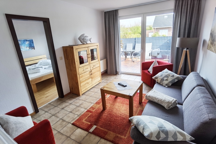 Ferienwohnungen im Ferienhaus Schillig | Wohnzimmer mit Sofa, 2 Sesseln, großem Fernseher und Tür zur Terrasse