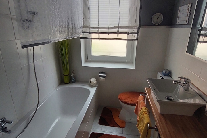 Badezimmer mit großen Fenster, Badewanne mit Duschrollo, Fön, verschiedene Duschartikel vorhanden, sowie Handtücher